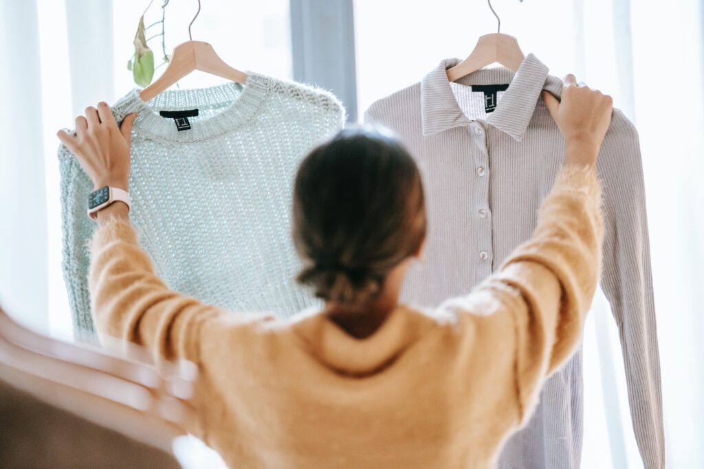Mujer sosteniendo dos prendas de ropa para identificar variantes de producto y registrarlas en Shopify.